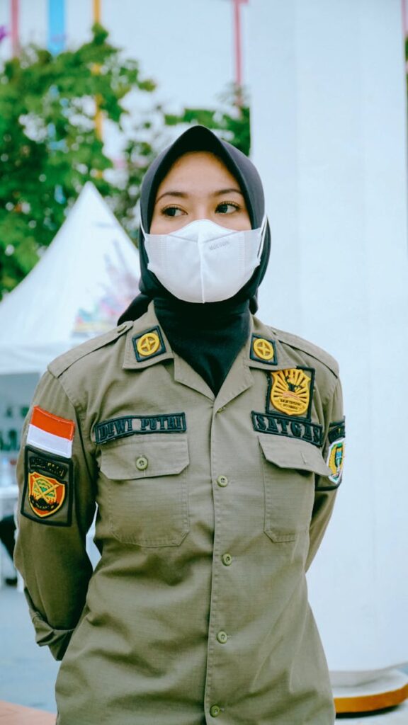 Indonesian policewoman wearing a hijab and face mask standing outdoors in uniform.