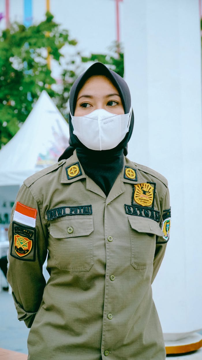Indonesian policewoman wearing a hijab and face mask standing outdoors in uniform.